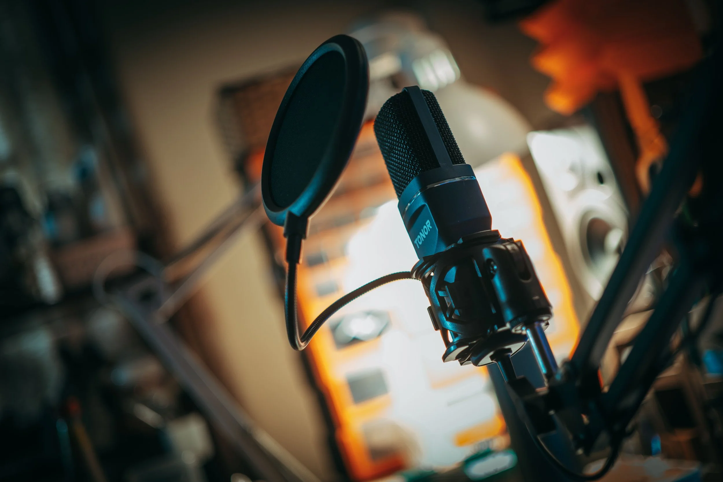 A microphone mounted on a stand in front of a computer screen displaying software or audio editing interface.