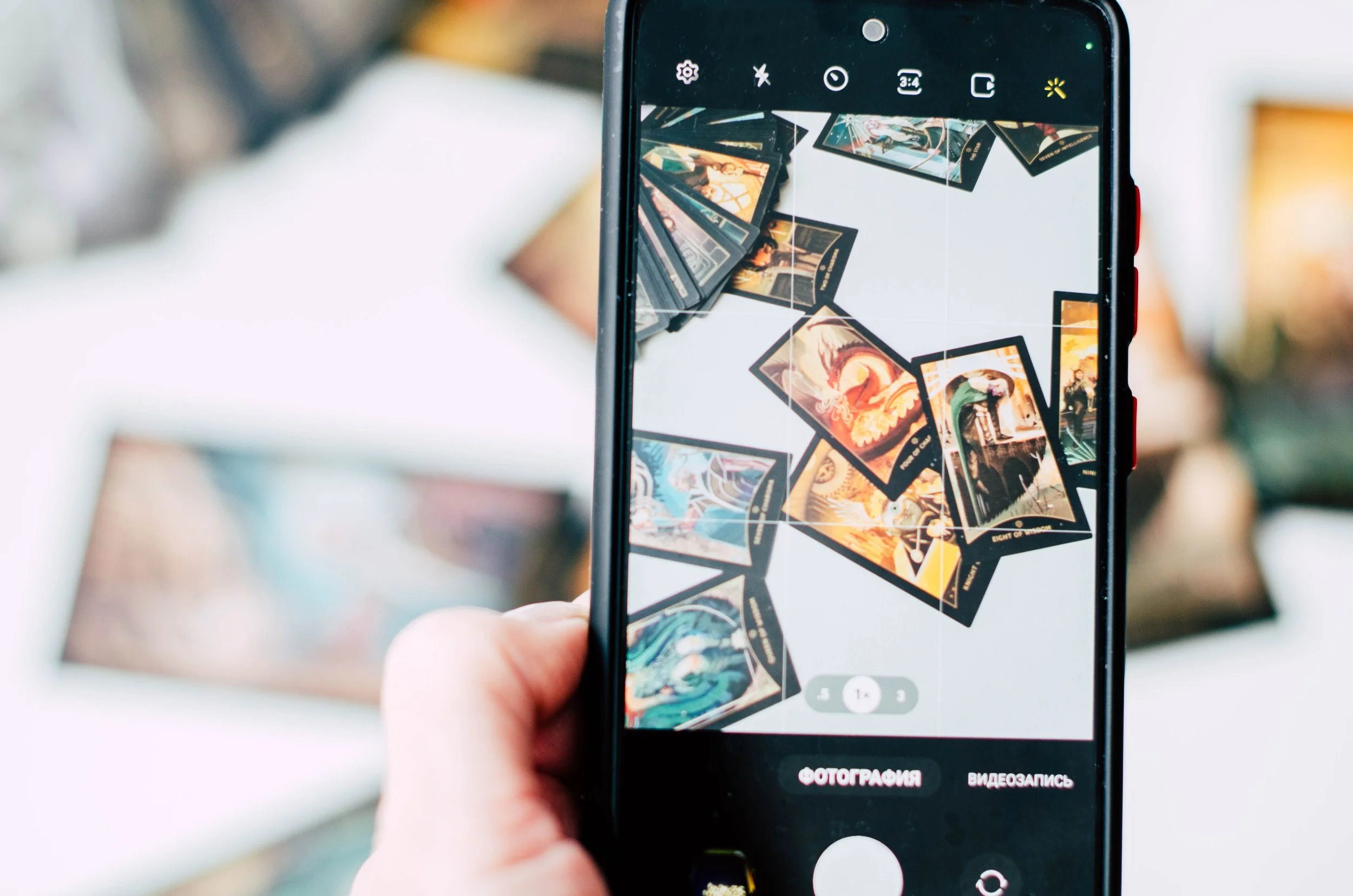 A person holding a smartphone taking a picture of trading cards laid out on a surface.