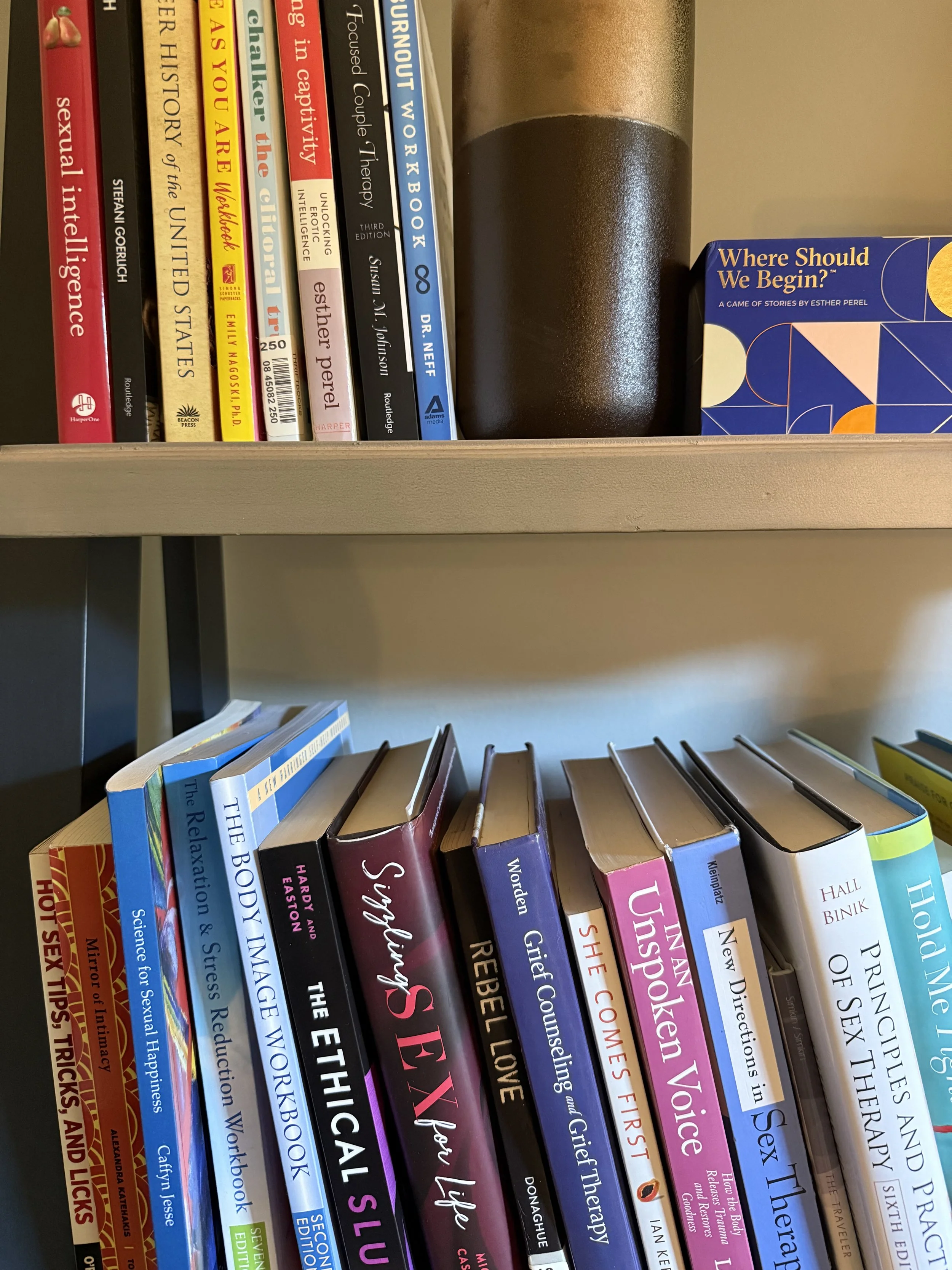 Shelf filled with books on various topics including sexual integrity, science, therapy, love, relationships, and sexuality, with a stack of books in the foreground.