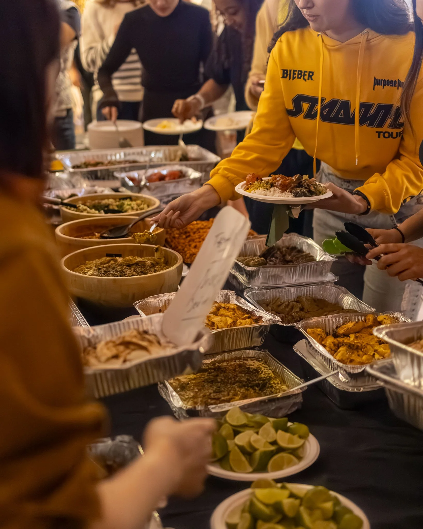 A group of people serving themselves food at a buffet table, with dishes including sliced limes in the foreground.