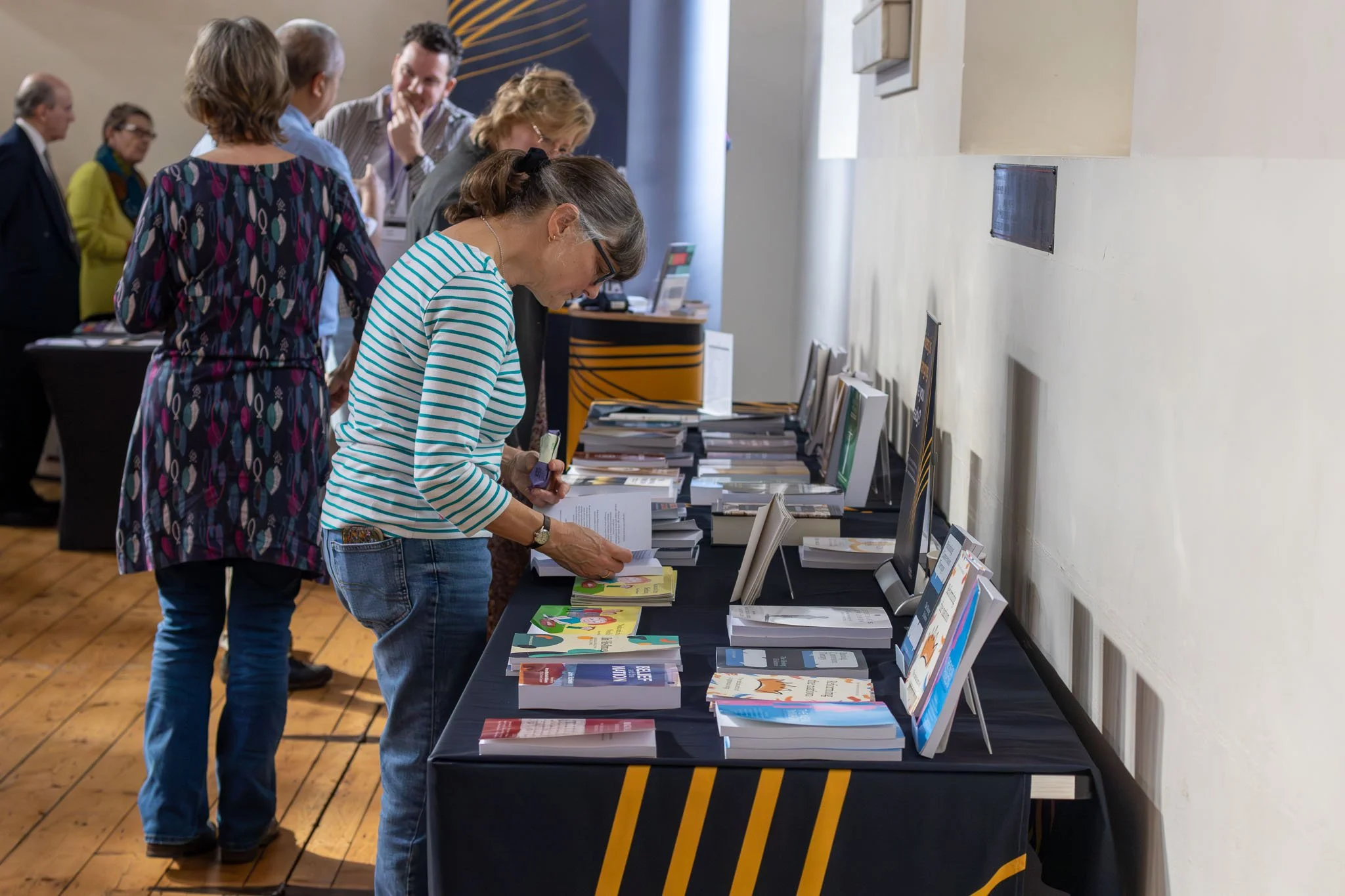 People browsing books at a conference or book fair, displaying various books on a long table.