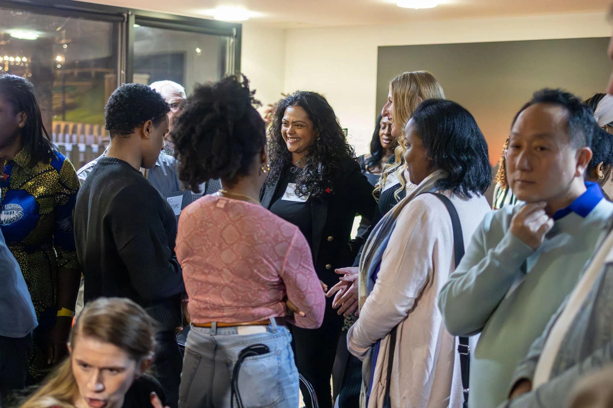 A group of diverse people interacting and talking in an indoor setting during an event, with some wearing name tags.
