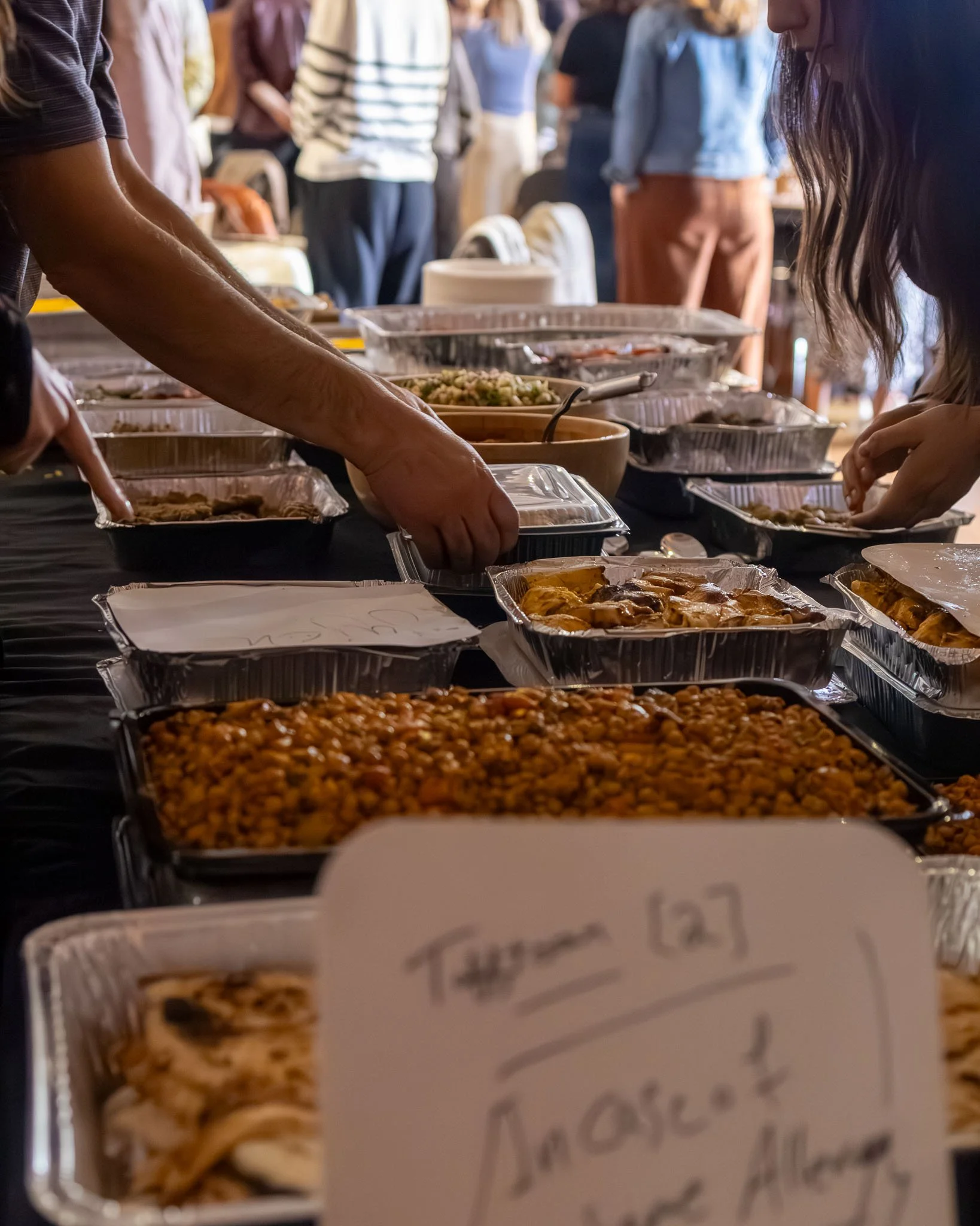 People setting up food from trays at a buffet table during an event.