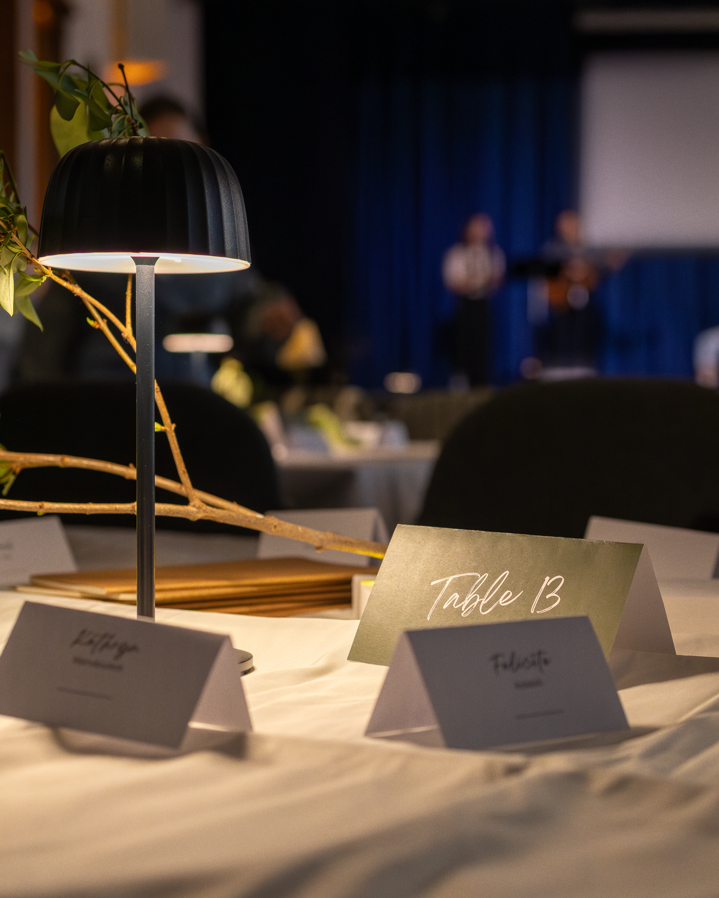 Close-up of table number sign labeled "Table 13" with blurred people in the background during an indoor event.