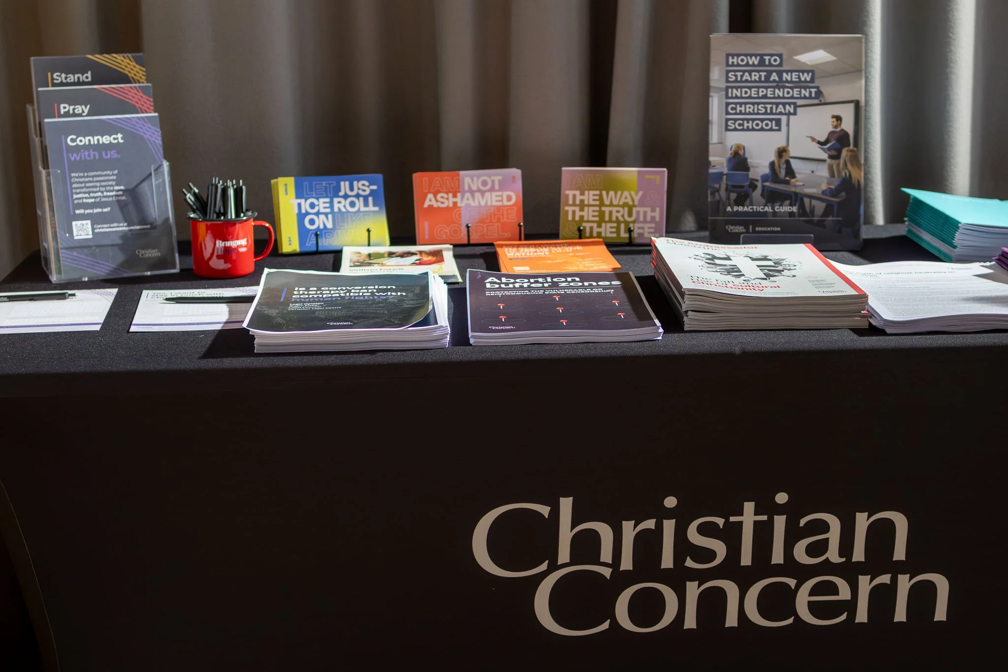 Display table with religious pamphlets, books, and brochures about starting Christian schools, abortion, and faith-based topics at Christian conference.