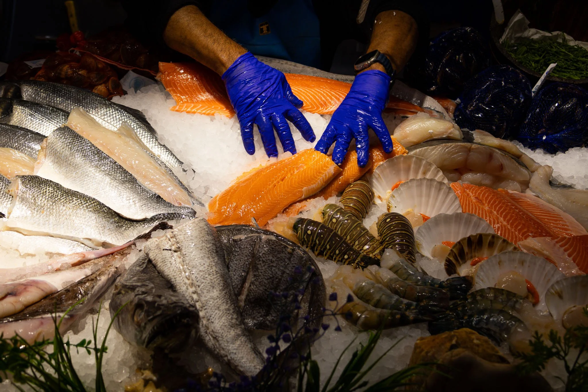 A person wearing blue gloves using a knife to cut salmon and other seafood on a bed of crushed ice at Borough Market.