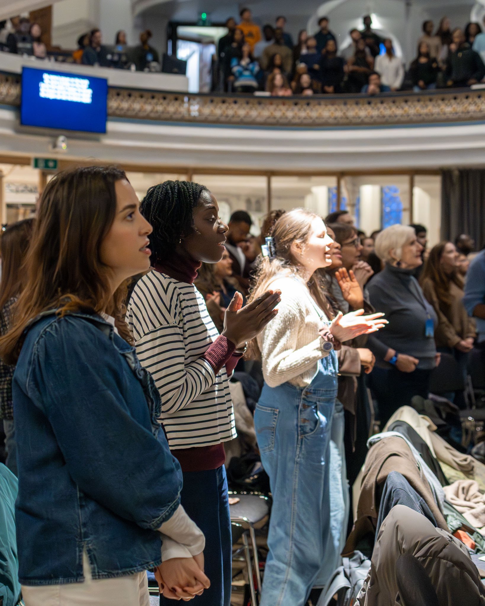 People attending church, standing and sitting, with some clapping and showing engaged expressions.