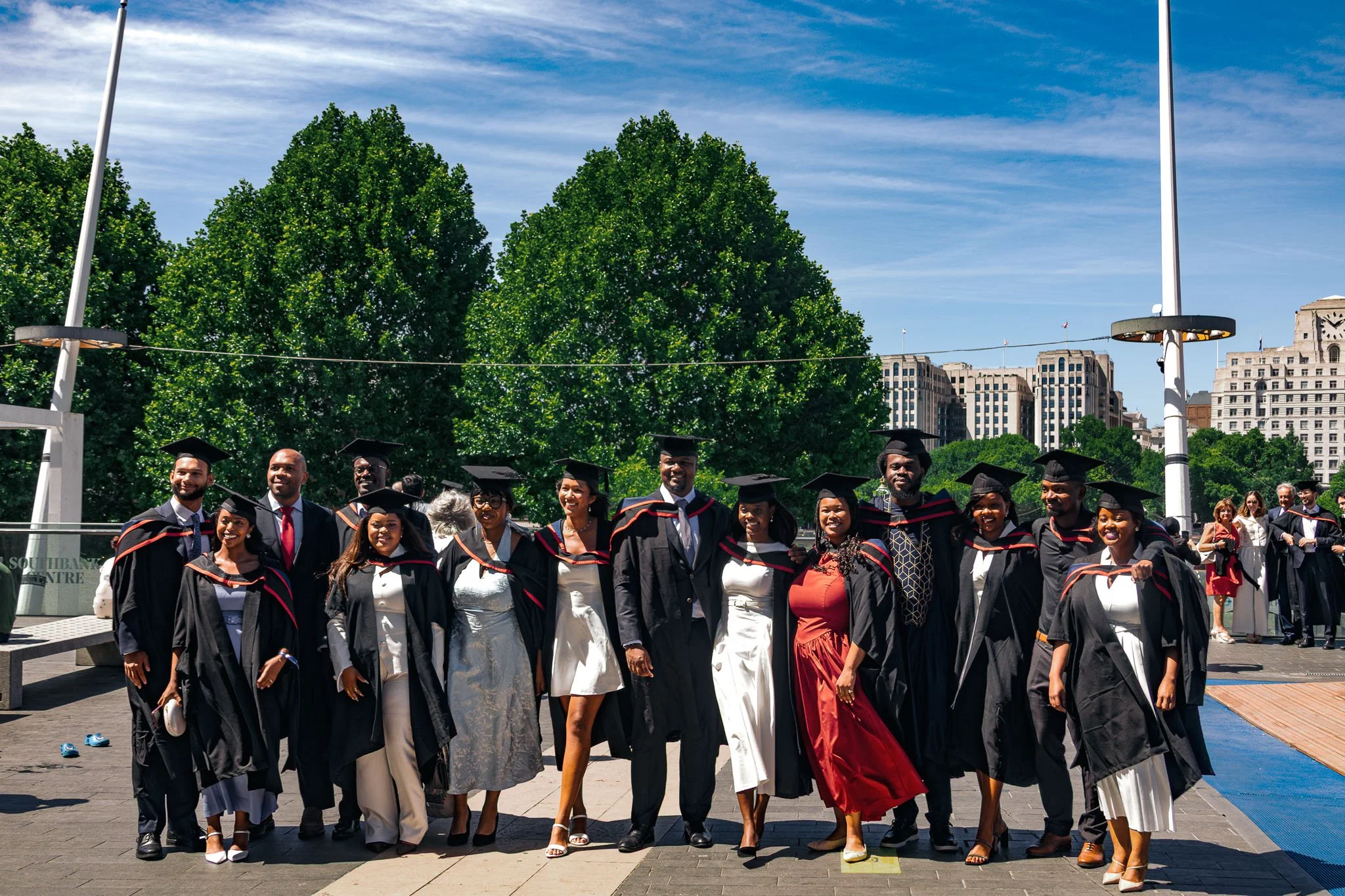 A group of diverse graduates in caps and gowns smiling outside during a graduation ceremony.