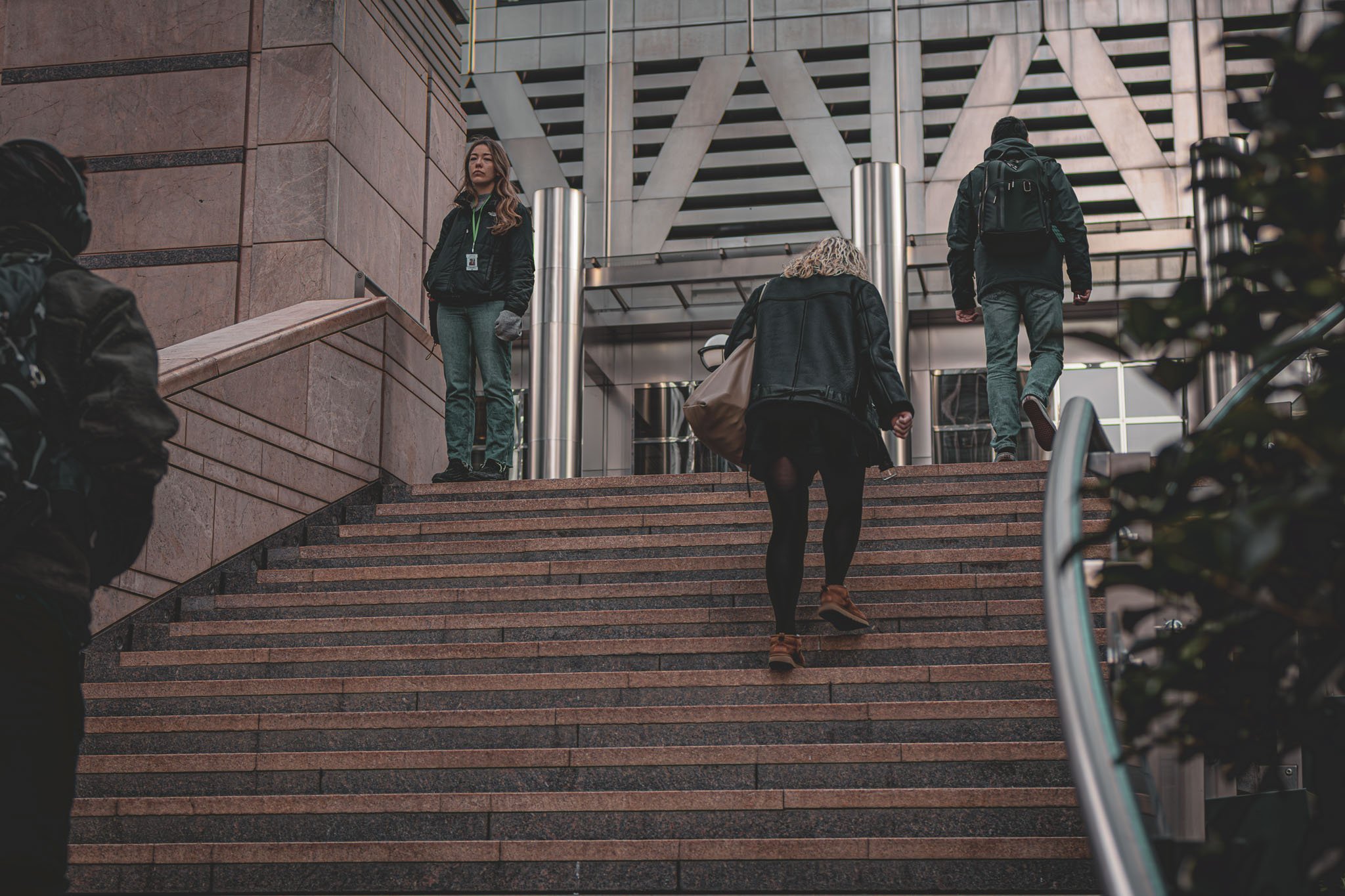 People walking up and down outside a modern building with staircase and glass entrance doors.