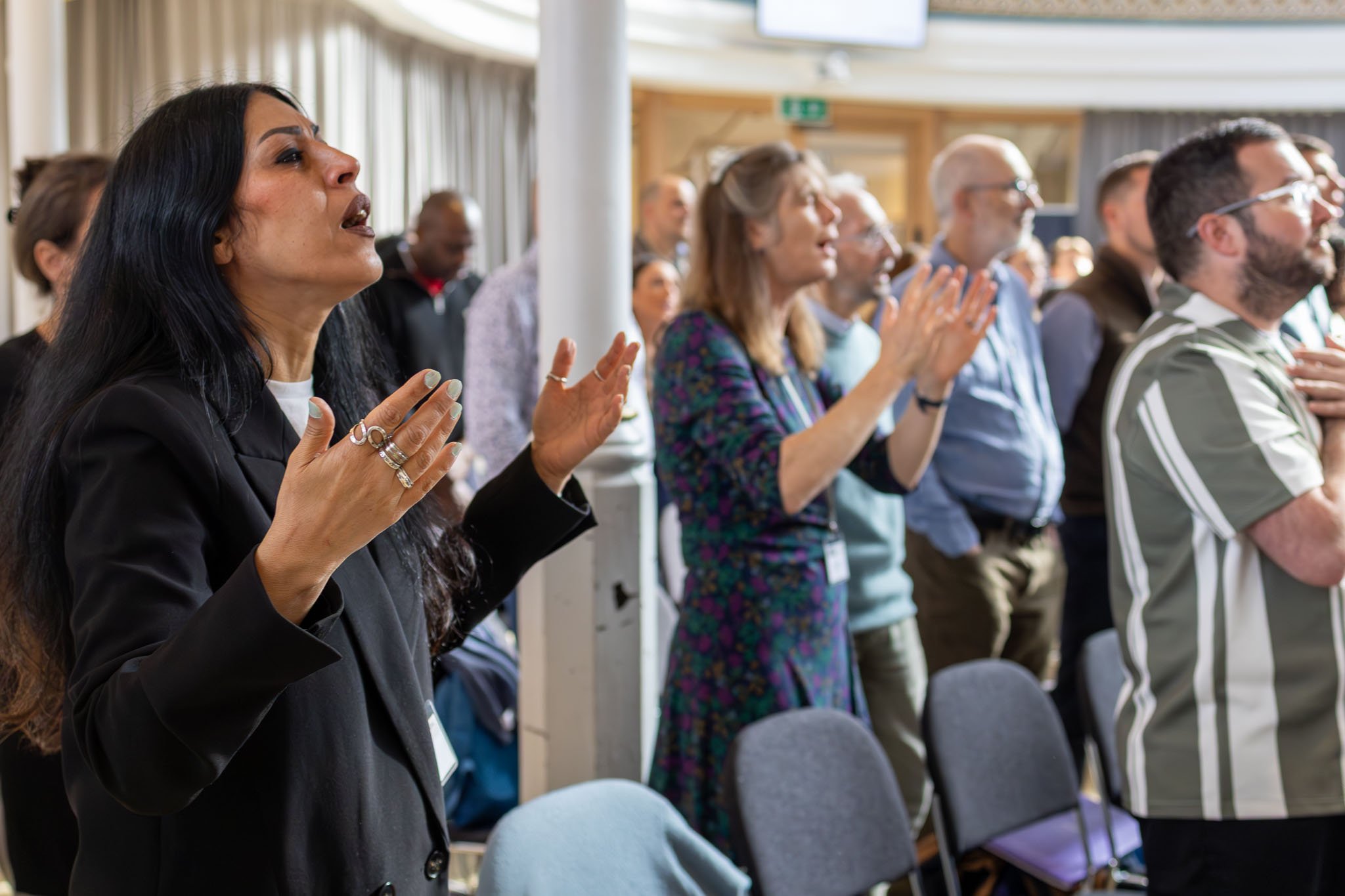Group of diverse people standing, praying, and raising their hands in what appears to be a conference or church setting.