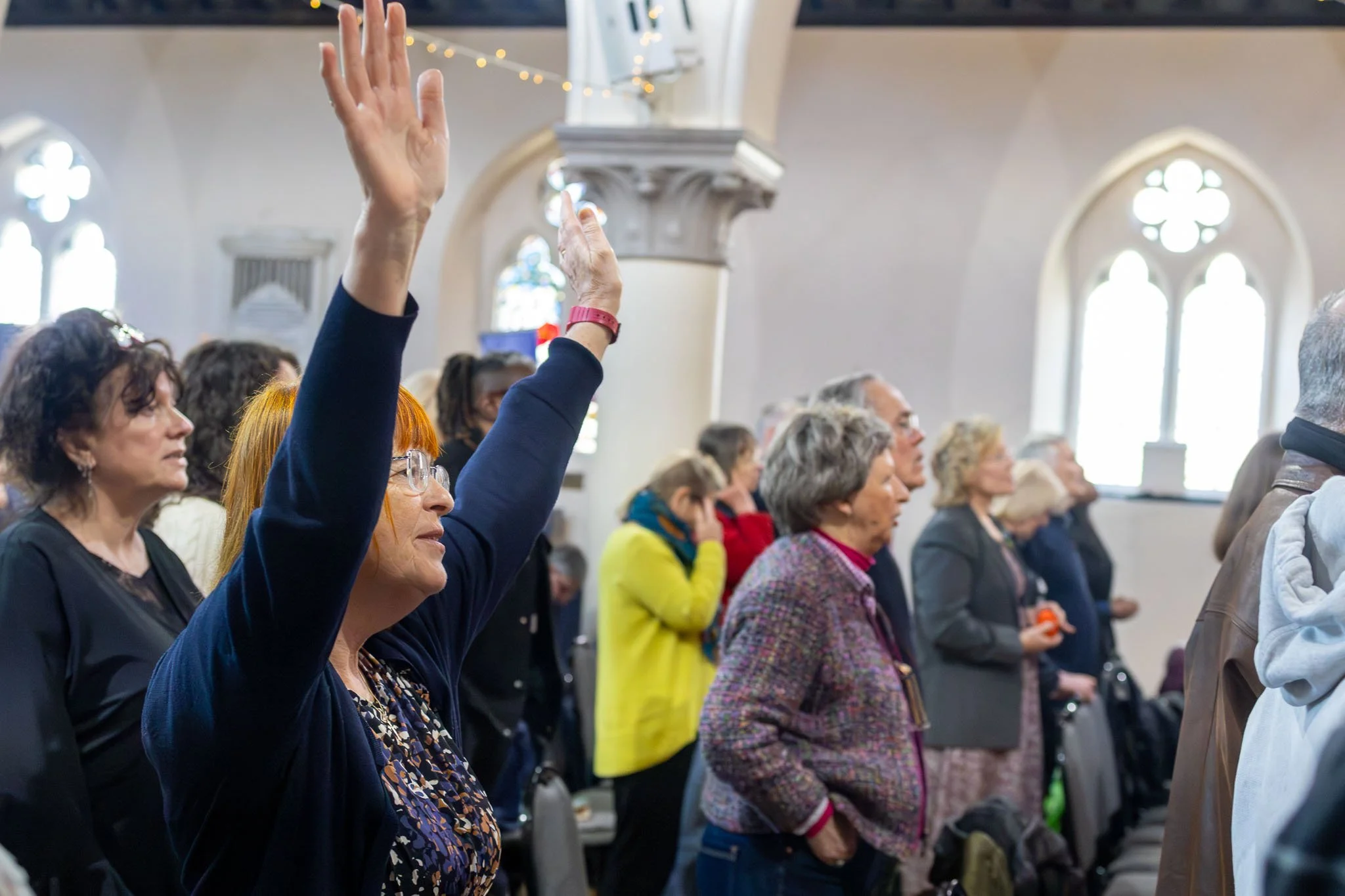 A diverse group of people in a church, with some individuals raising their hands during a religious service or event.