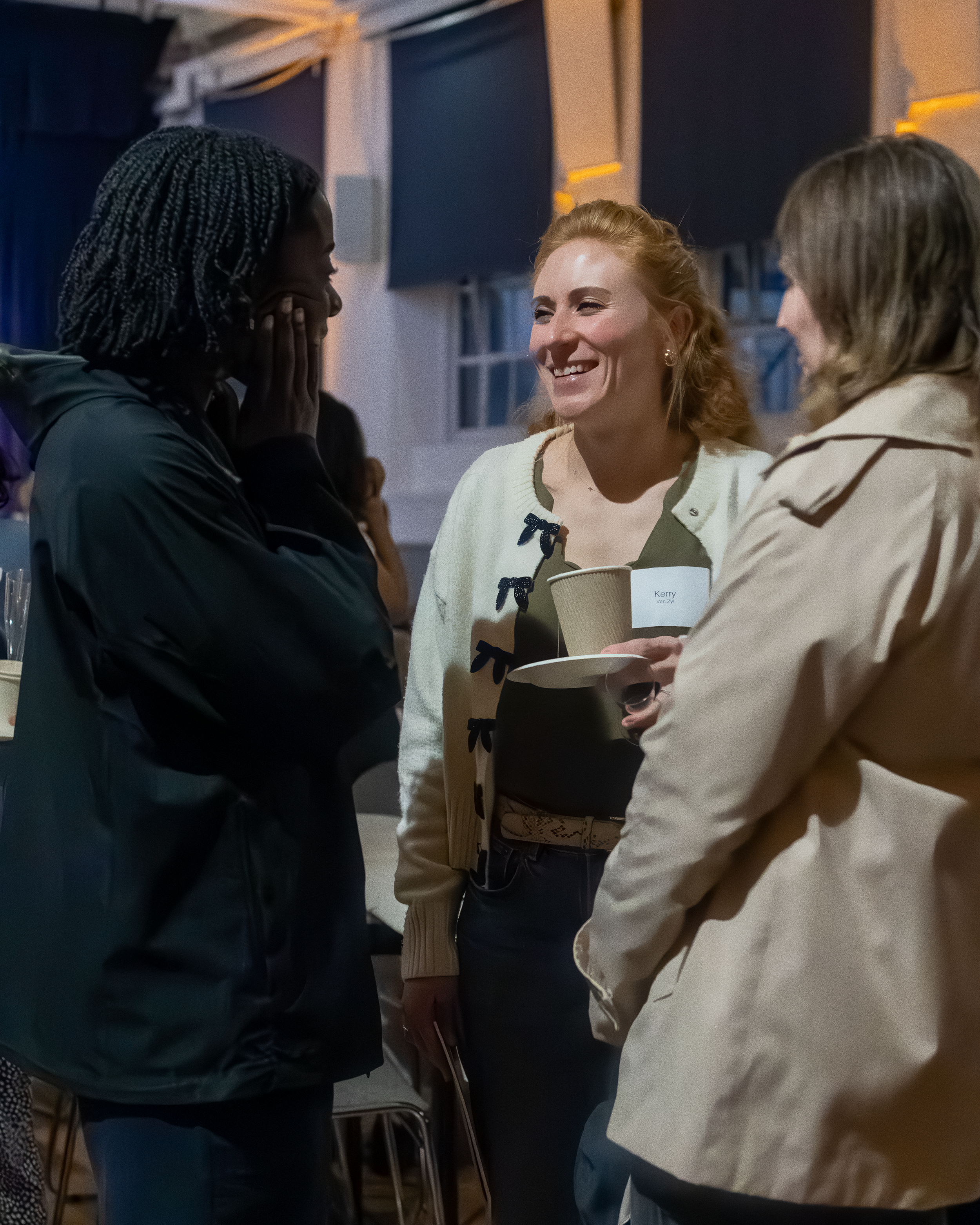 Three women engaged in conversation at a church event, with one woman smiling and holding a paper cup.