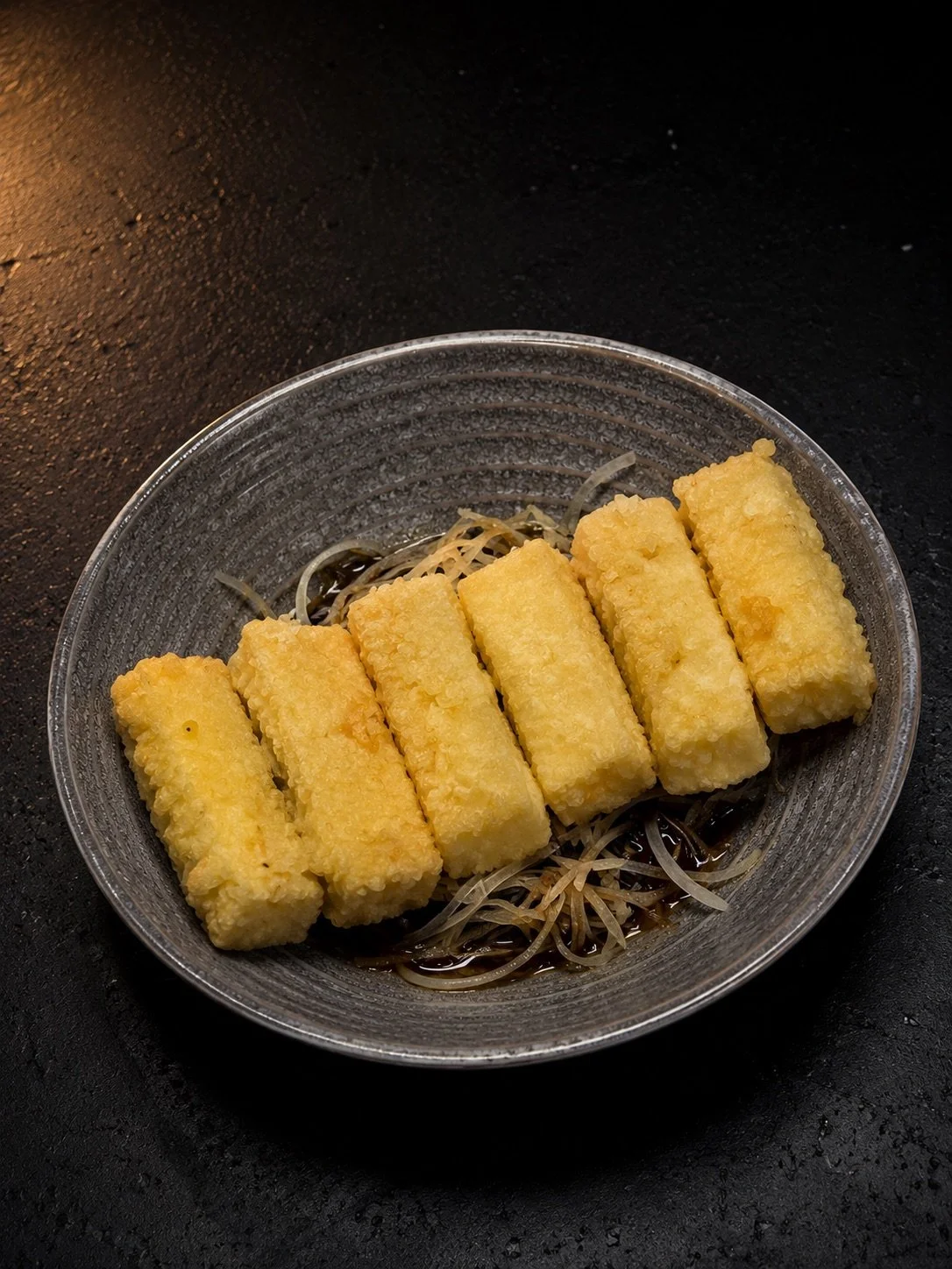 Fried fish sticks on a bed of bean sprouts with soy sauce in a glass bowl.