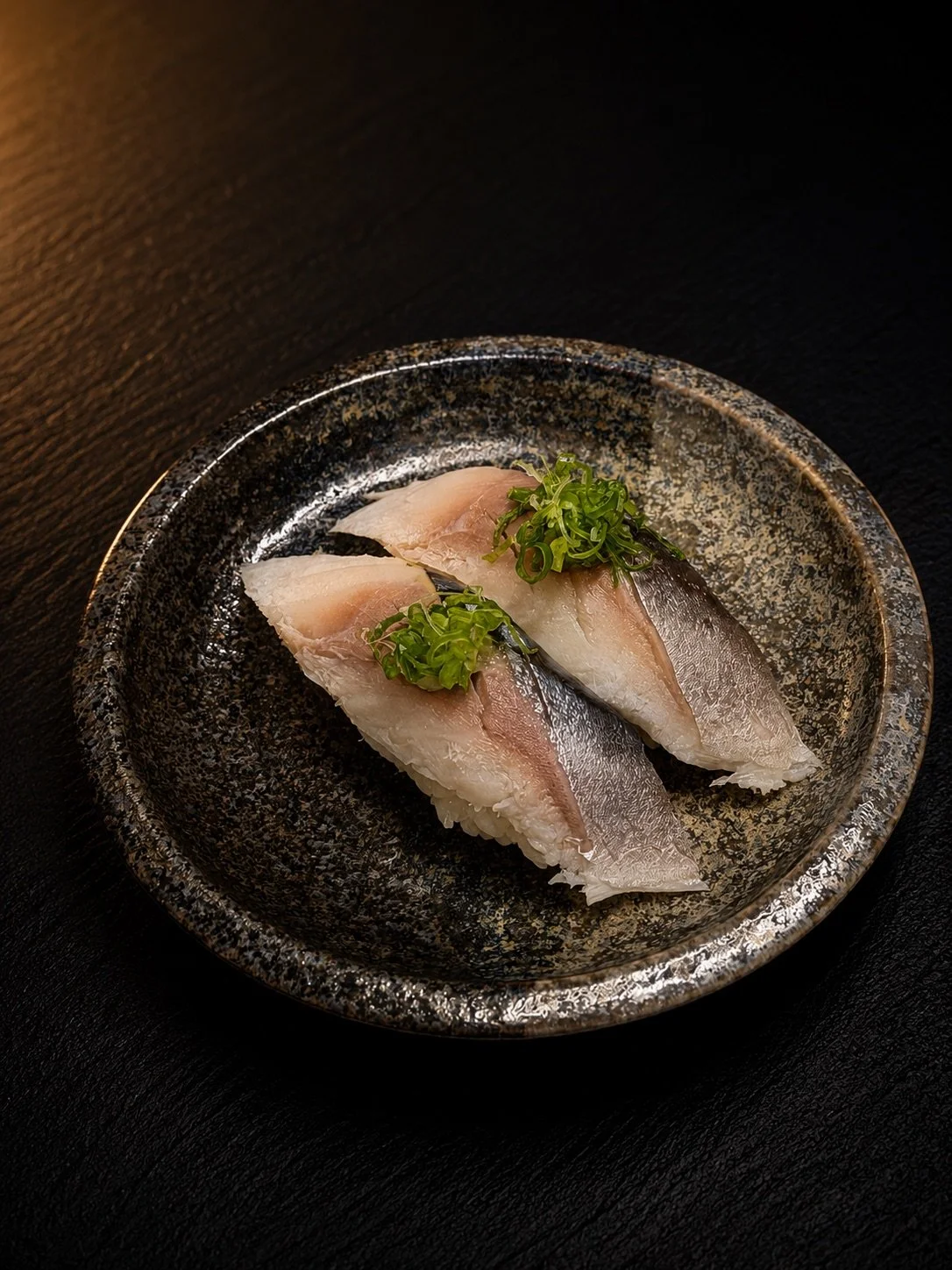 Two pieces of sashimi with green onions on a black and gold textured plate