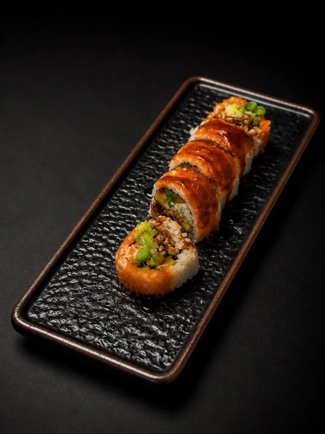 Sushi rolls on a black textured rectangular plate with dark background.