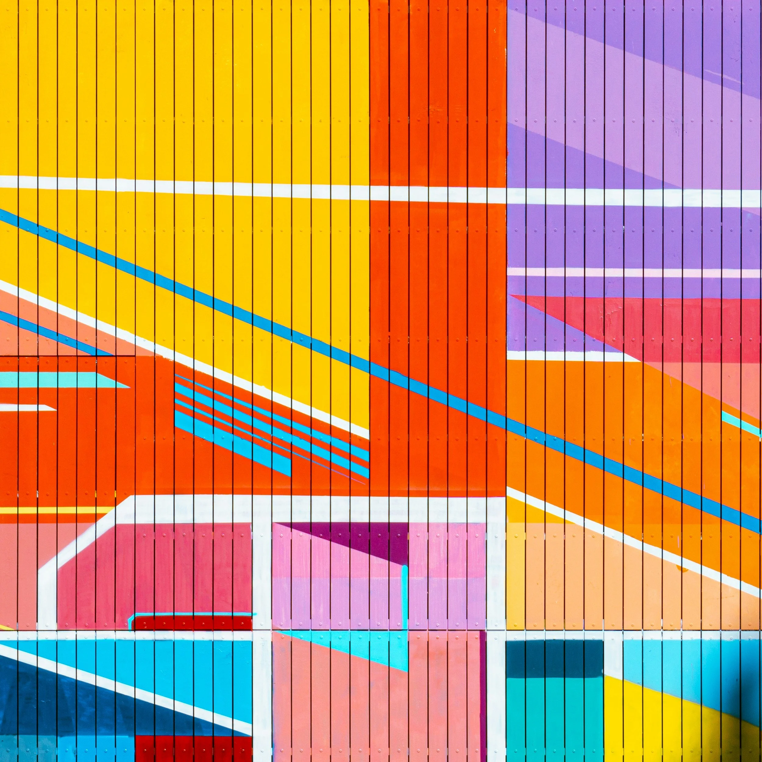 Colorful, geometric wall mural with vertical, diagonal, and horizontal lines, blocks, and shapes in yellow, red, orange, purple, pink, blue, and white.