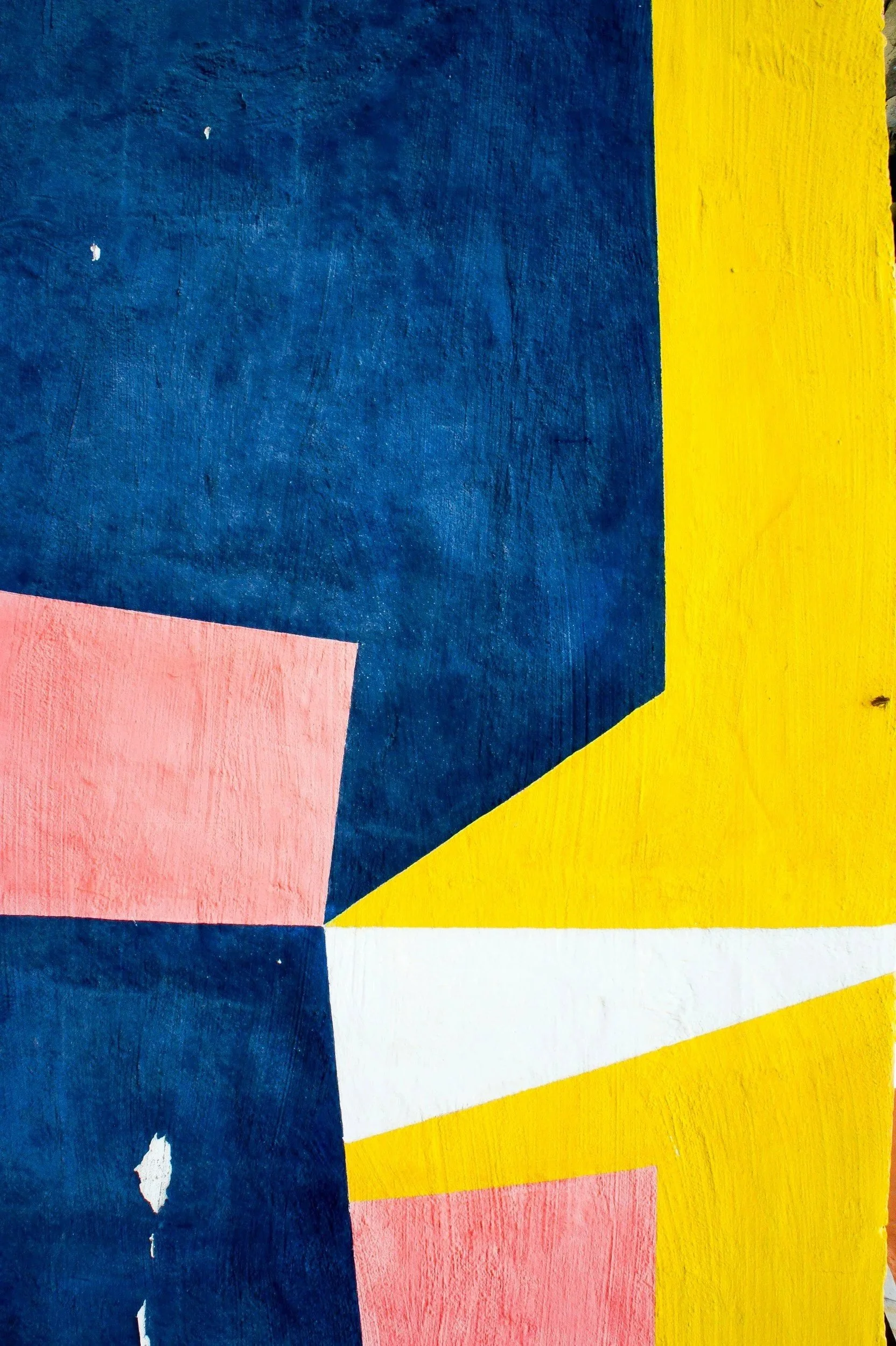 Close-up of a colorful geometric abstract painting with blue, yellow, pink, and white shapes on a wooden surface.