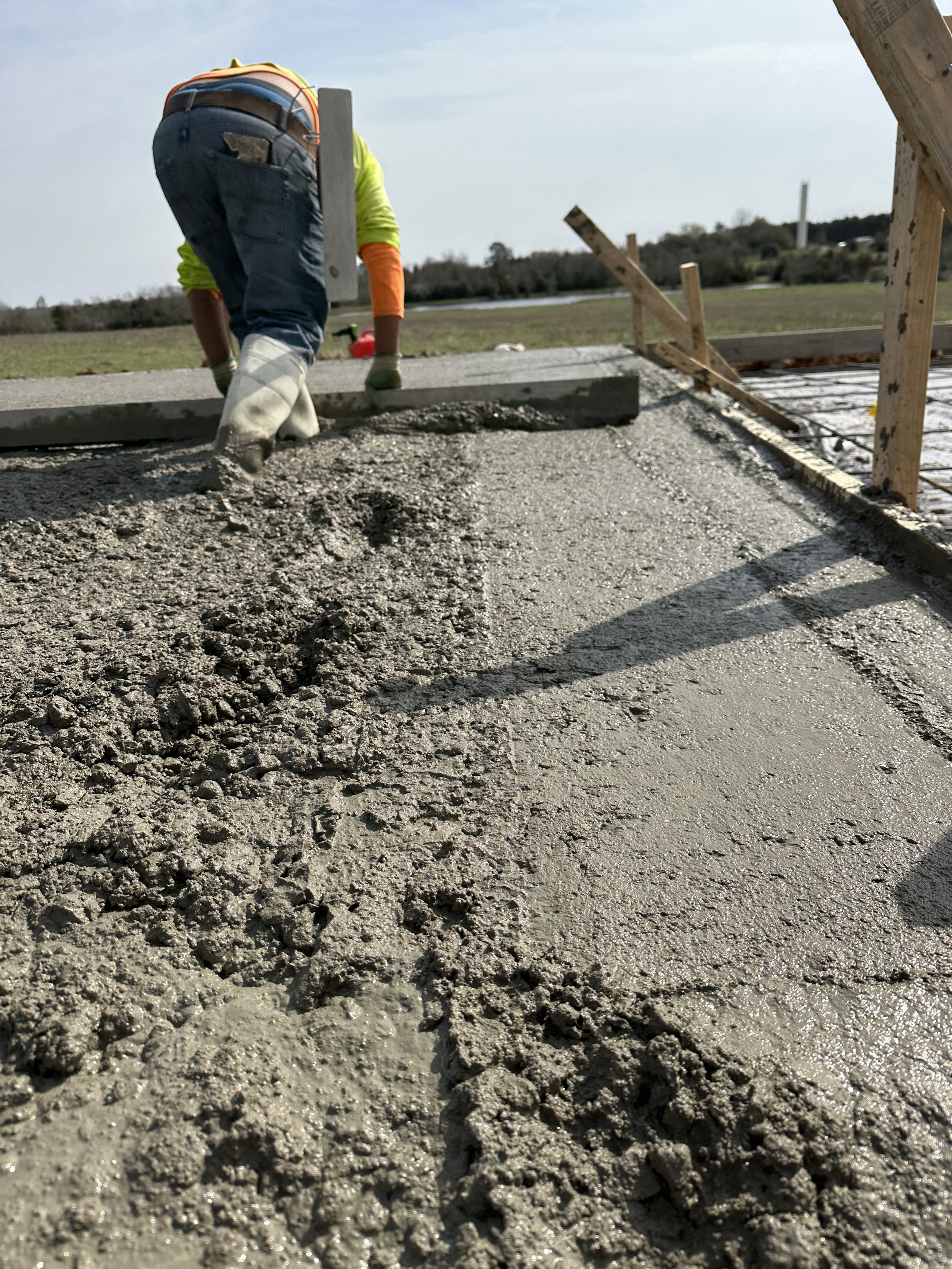 Construction worker pouring and smoothing wet concrete .