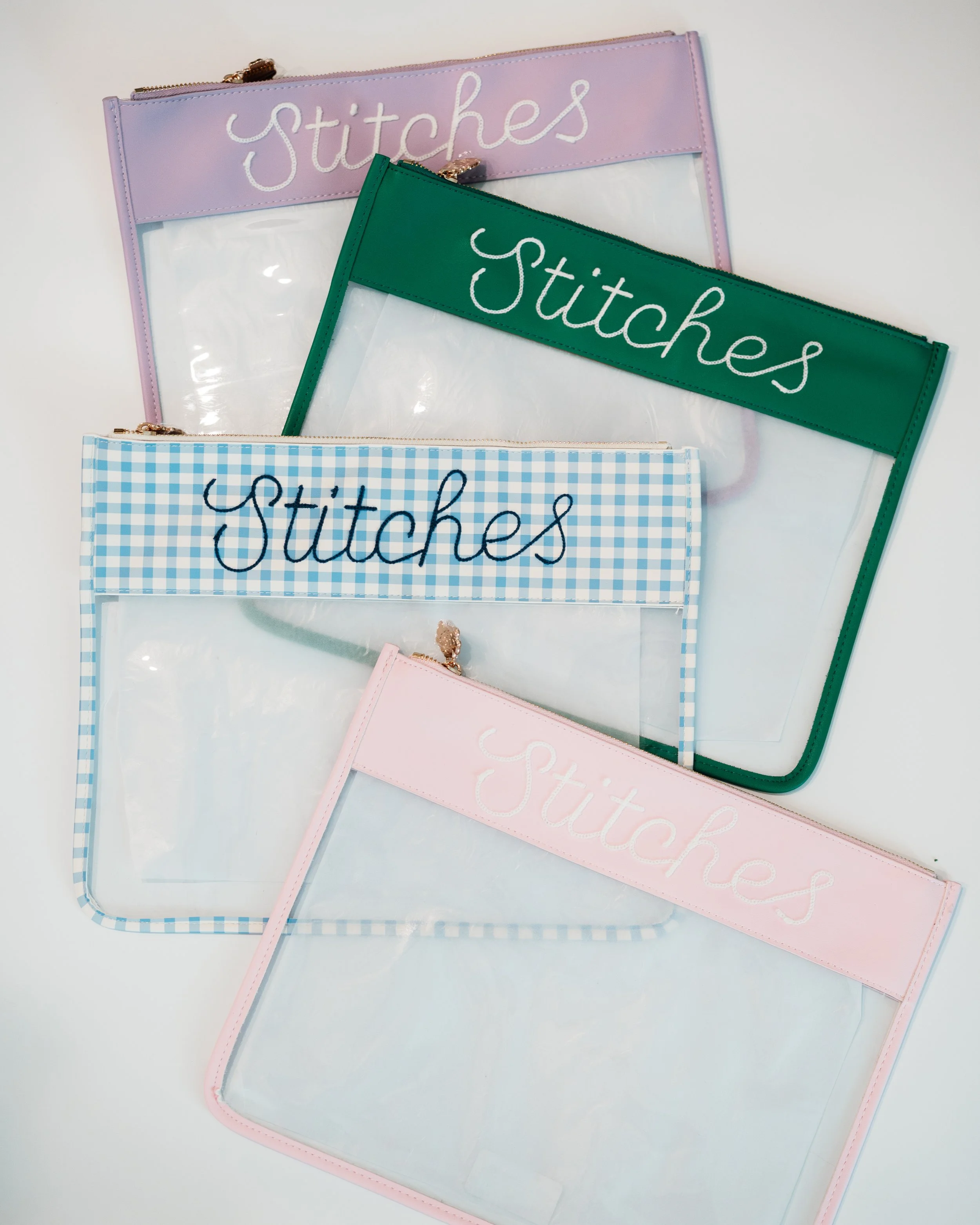 Three clear plastic storage pouches with colored borders and embroidered word "Stitches" in different colors and styles, placed overlapping on a white surface.