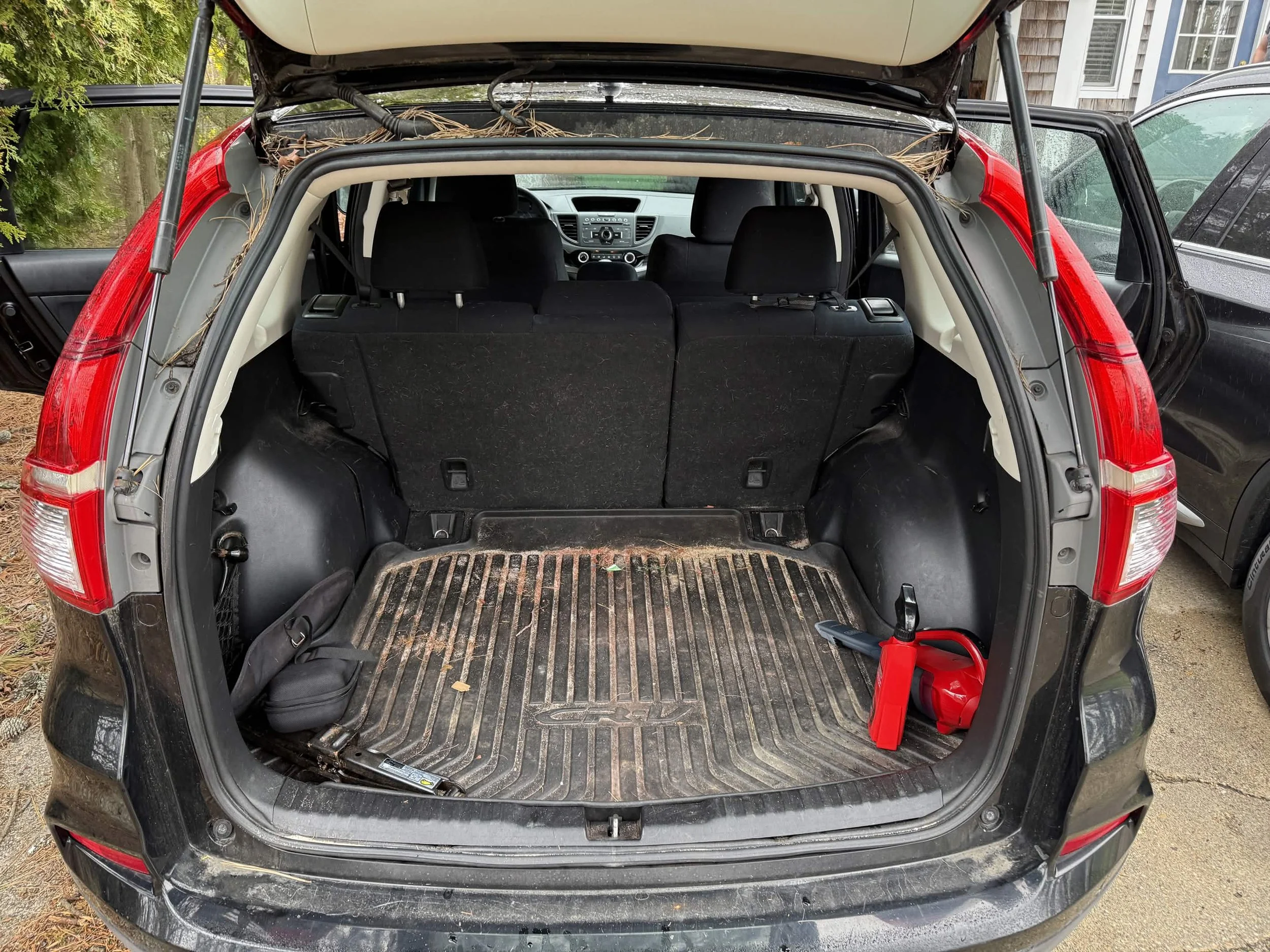 Open trunk of a black SUV with a rubber cargo mat, some leaves, a small black bag, a red fire extinguisher, and a red warning triangle.