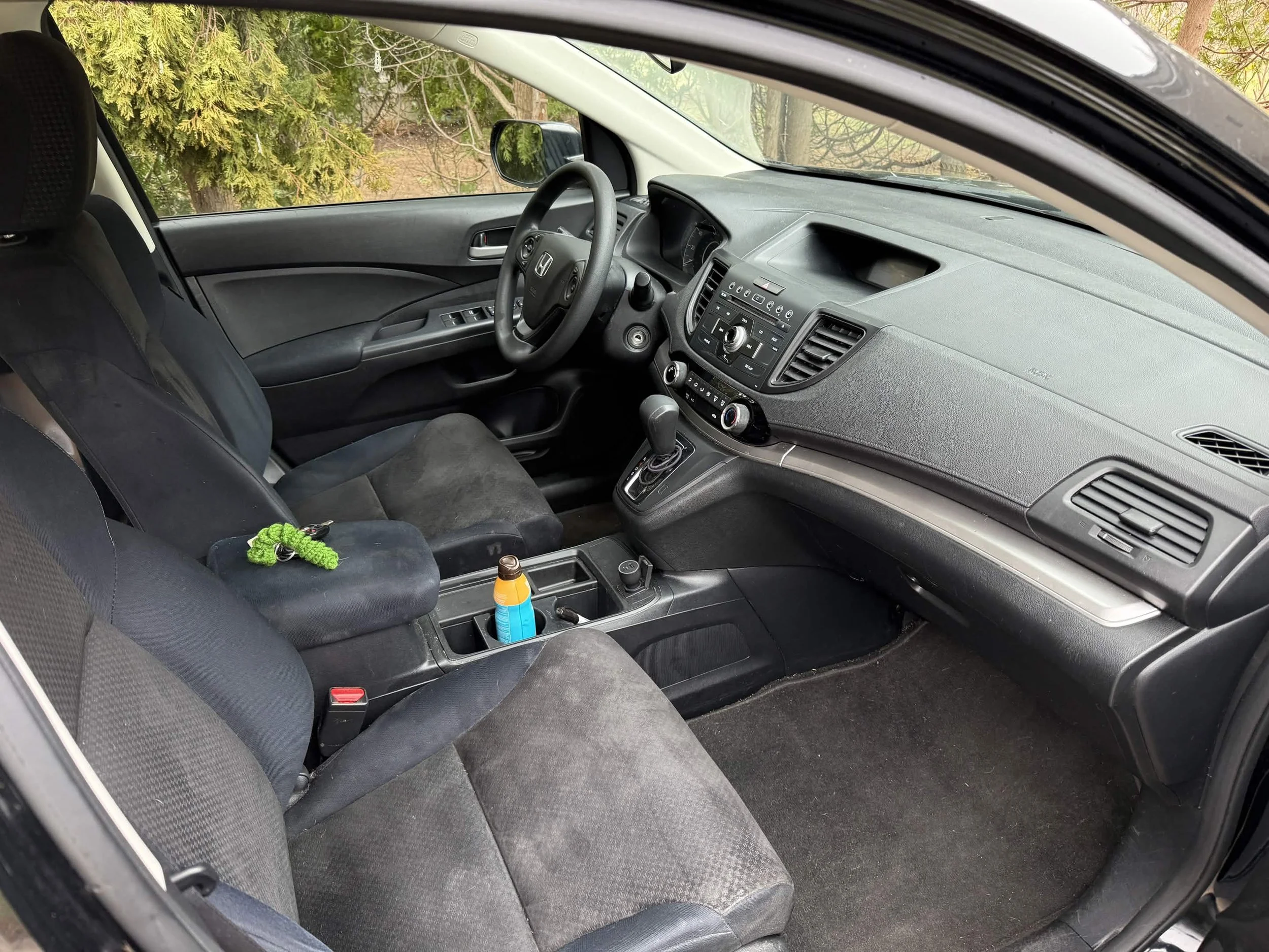 Interior of a car showing the front seats, dashboard, steering wheel, gear shift, and center console with a bottle and green rope on the console.