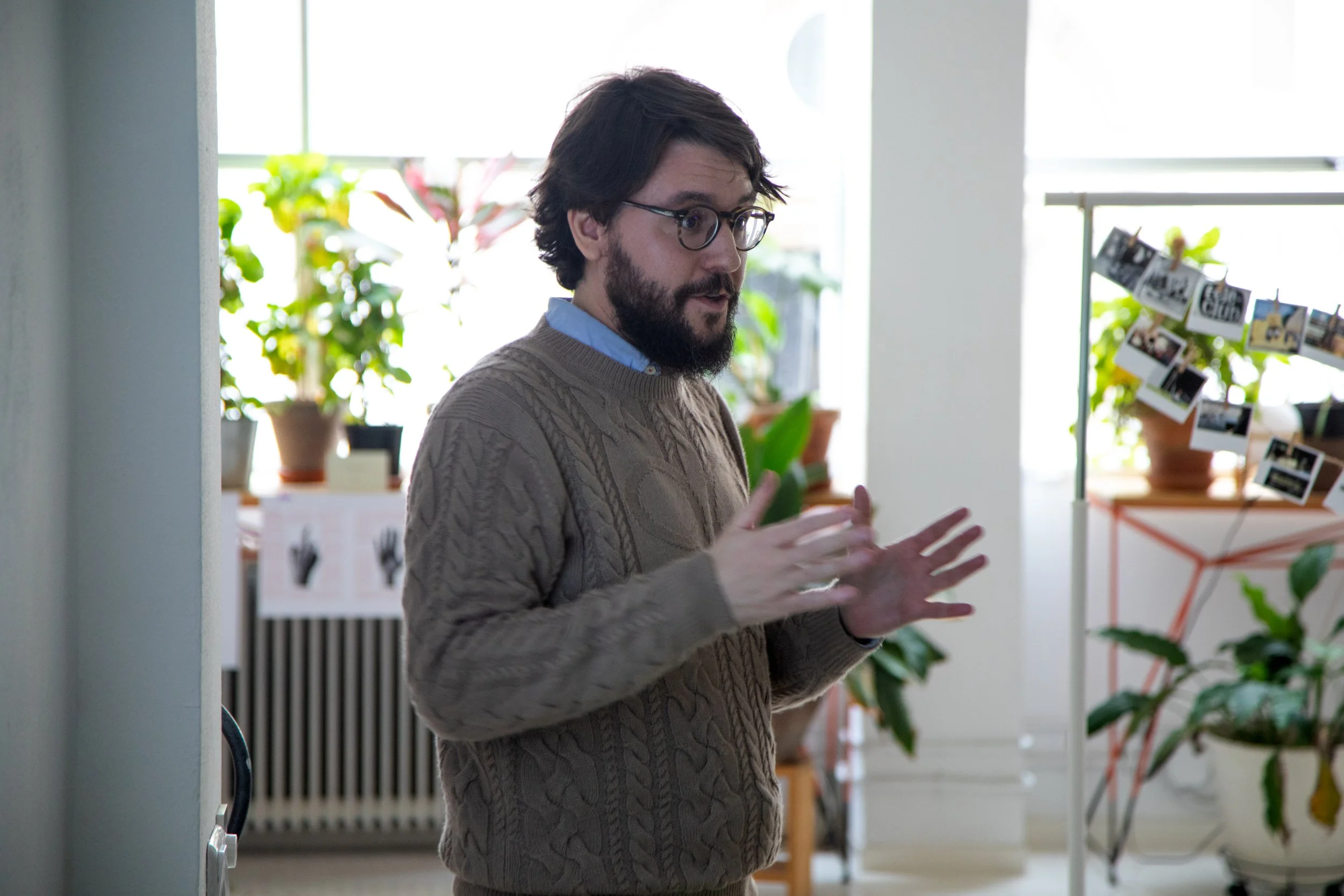 Hombre con gafas y barba hablando en una habitación con plantas y fotos en exhibición.