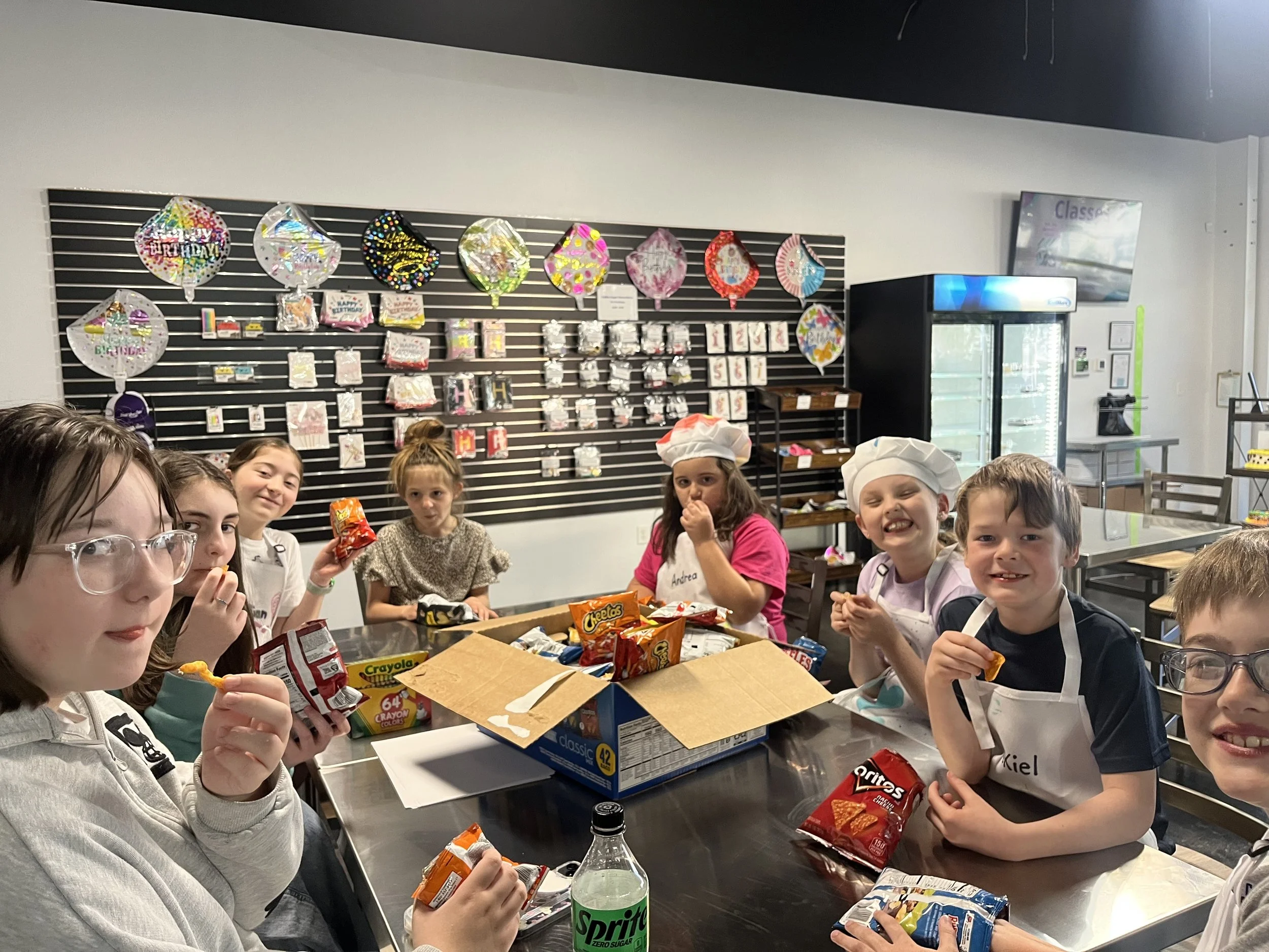 Children gathered around a table eating snacks with Halloween decorations behind them.