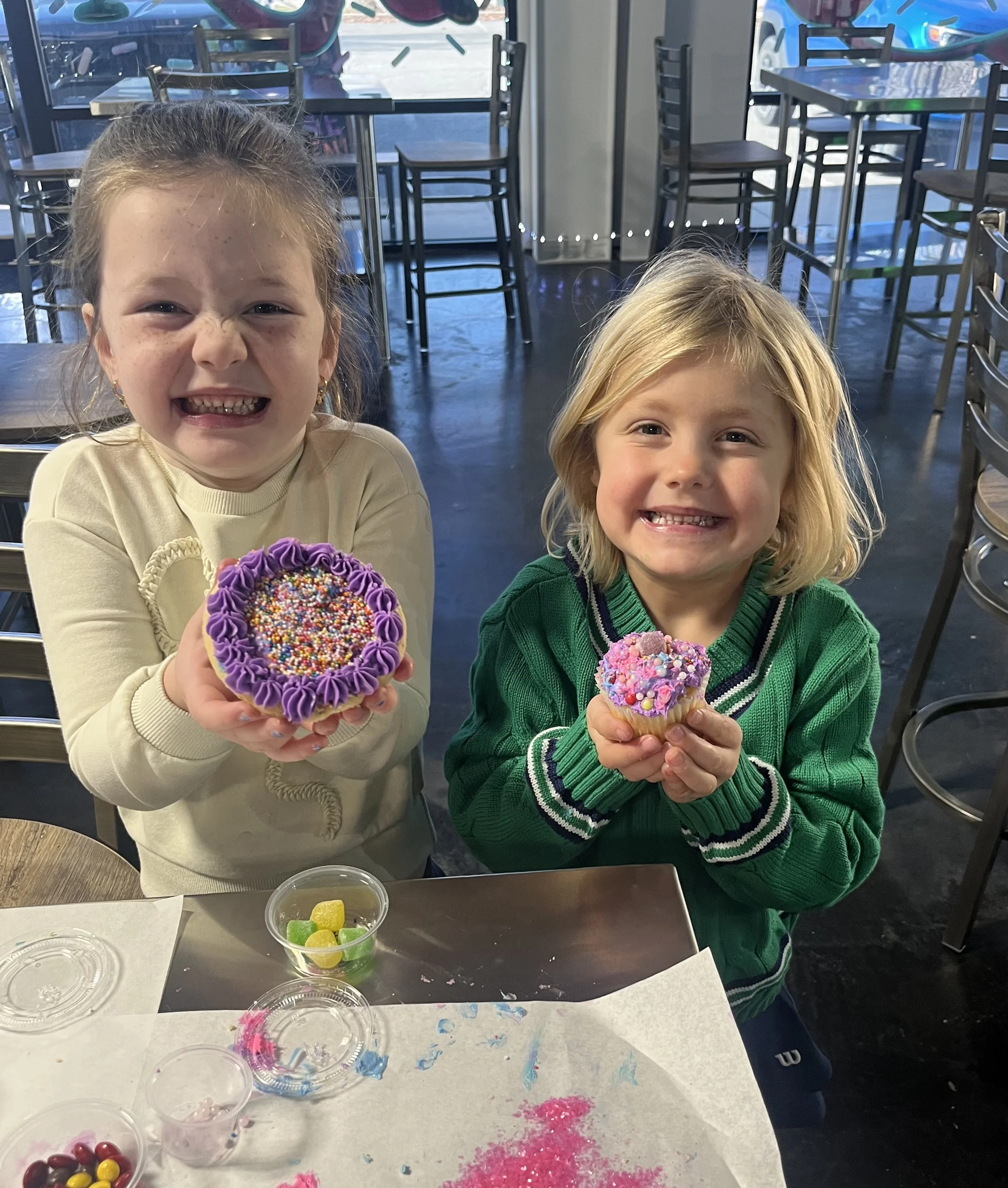 Two smiling young children, showing off their decorated cookie and cupcake full of frosting and sprinkles