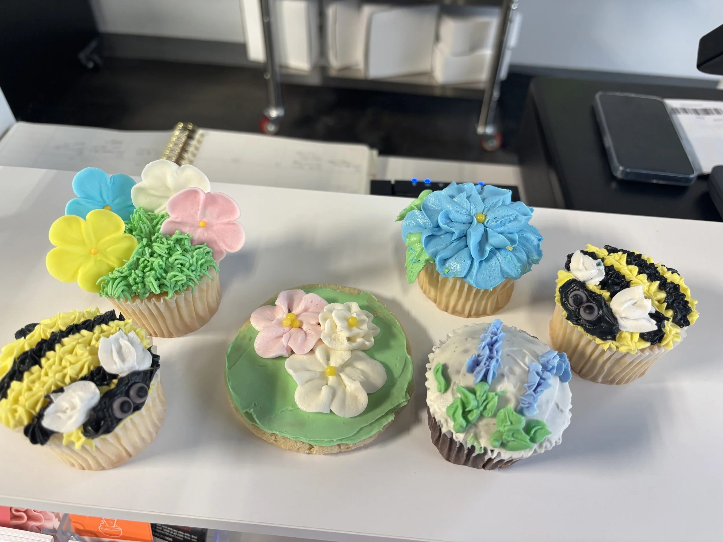 Assorted decorated cupcakes with colorful frosting flowers and sprinkles on a display table.