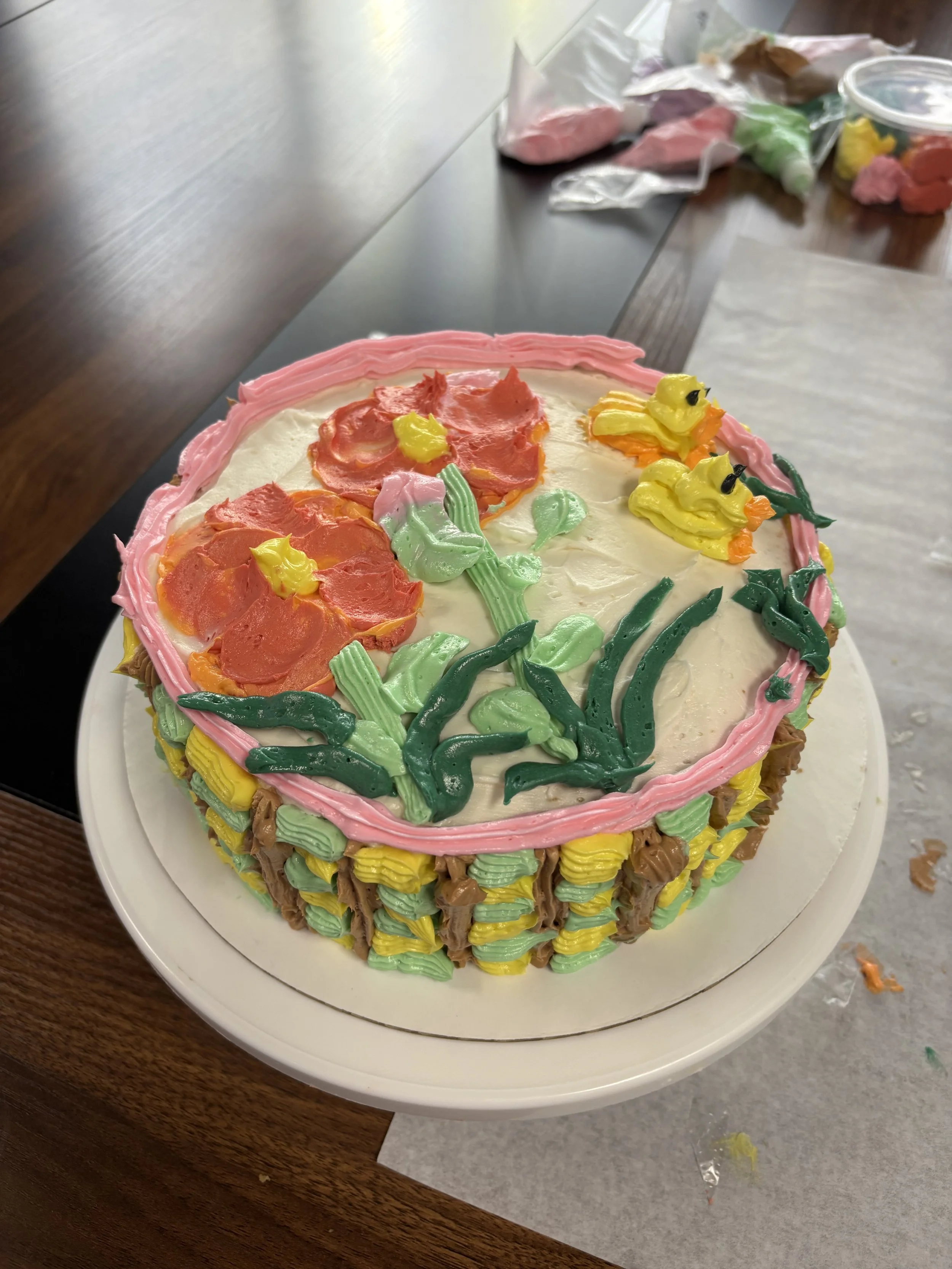 Decorated cake with yellow duck and duckling toppers, pink flowers, and green leaves made of icing.