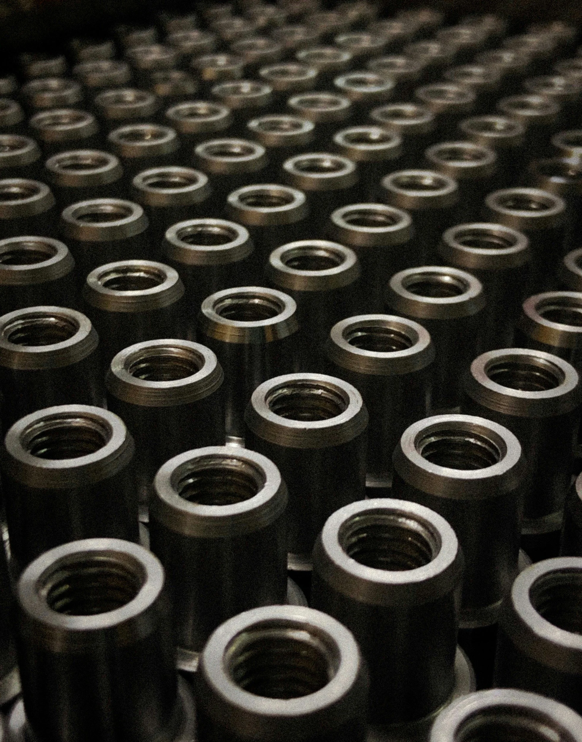 Multiple metal threaded cylindrical components arranged in rows.