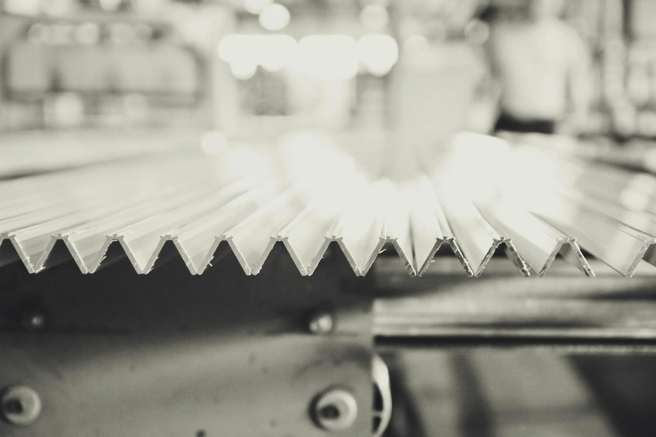 Close-up of metallic corrugated sheets in a manufacturing or industrial setting, with blurred background.