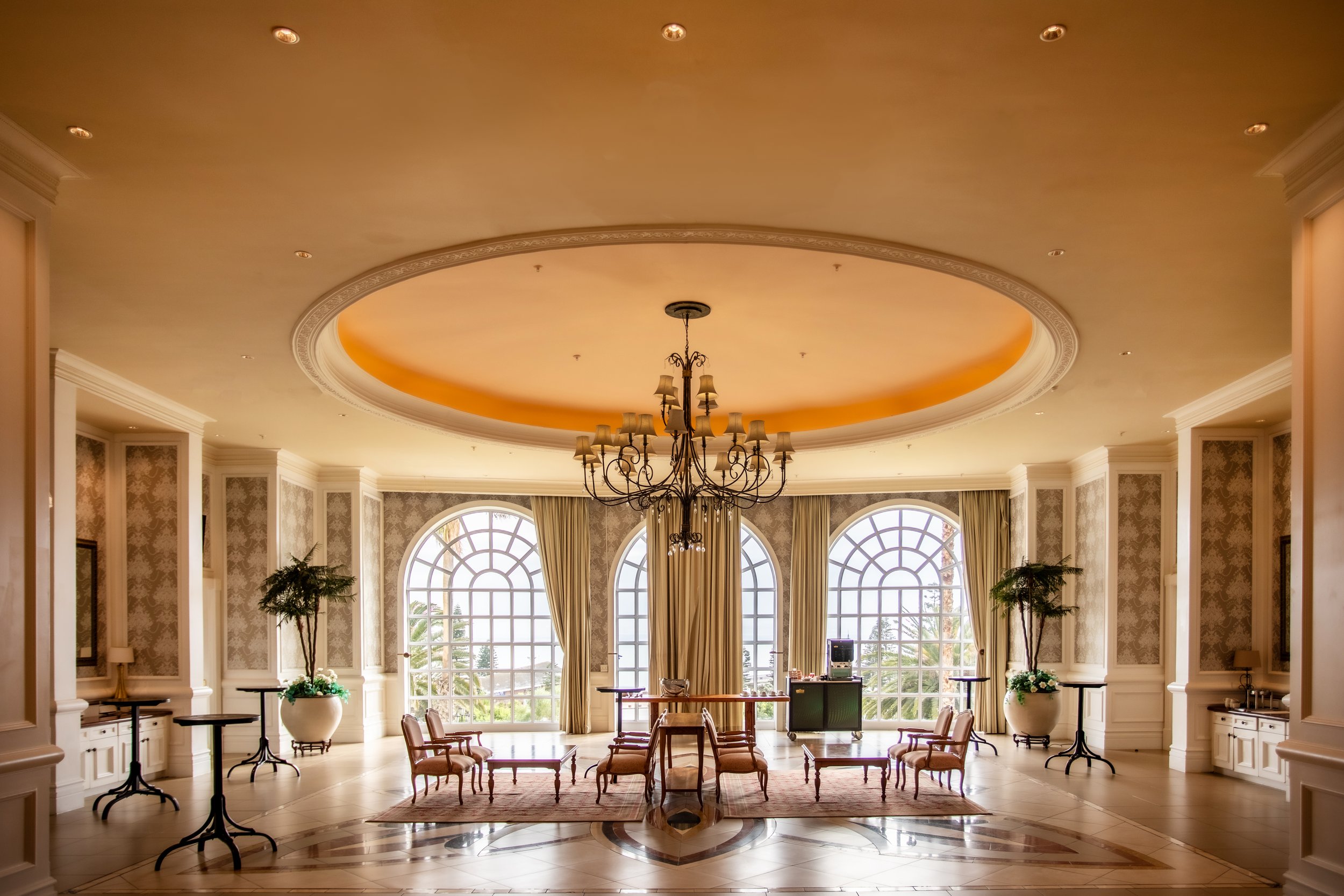 Elegant interior room with large arched windows, a chandelier, and tables and chairs.