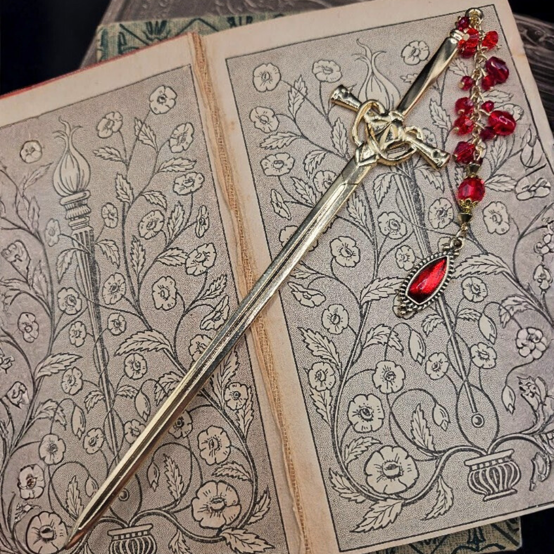 Open coloring book with floral designs, a decorative sword bookmark and a red pendant with matching beads.