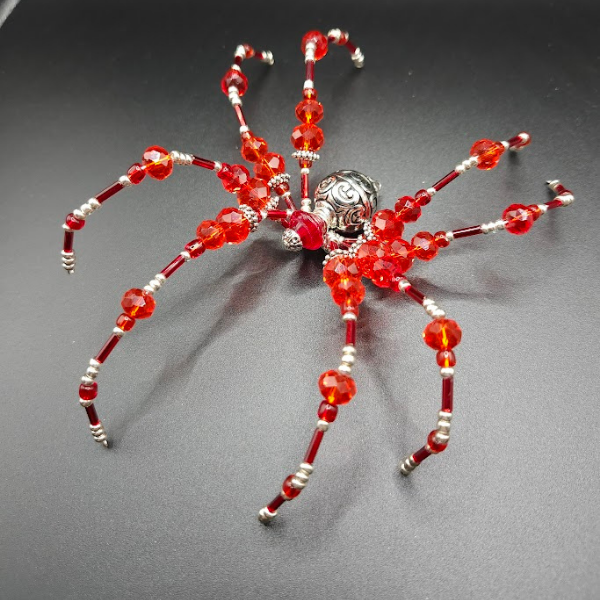 Decorative spider made of red beads and silver accents on a black background.