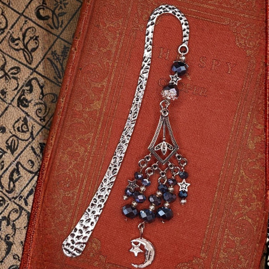 Decorative bookmark with celestial-themed charms, including a moon and star, on a textured red book cover.