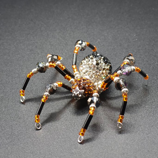 Beaded spider craft with a black body and shiny bead details on a gray surface.