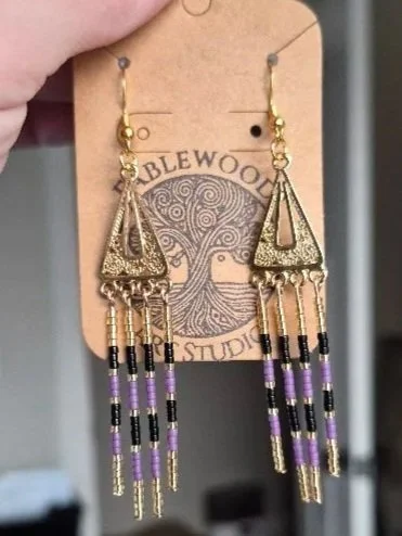 Gold and purple beaded dangle earrings on a display card with a tree logo and the word 'Fablewood Art Studio'