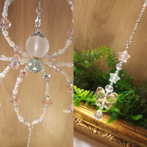 Close-up of a beaded spider, one with a large frosted bead and the other with star-shaped and butterfly-shaped charms, displayed with a wooden background and green plants.