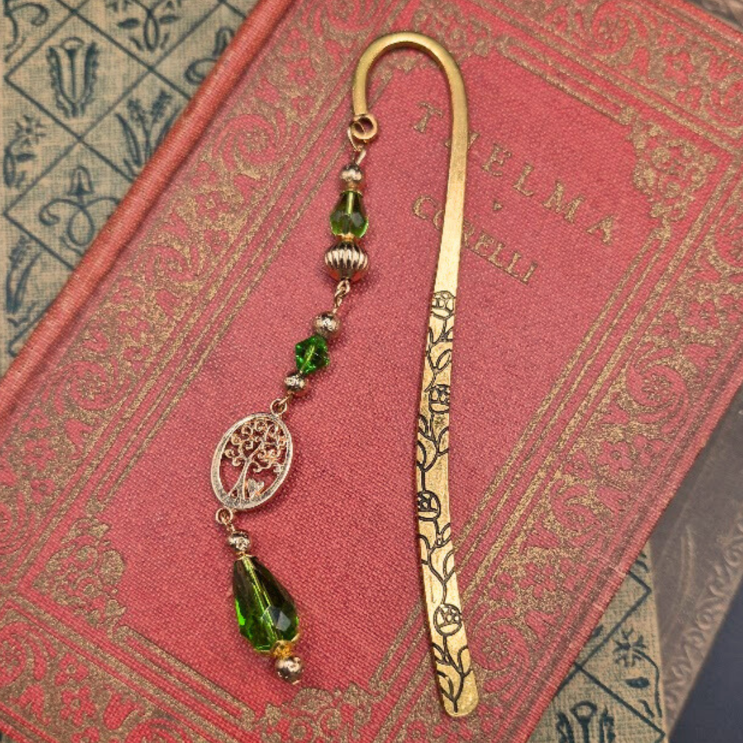 A decorative bookmark with green beads and a tree of life charm, resting on a pink book.