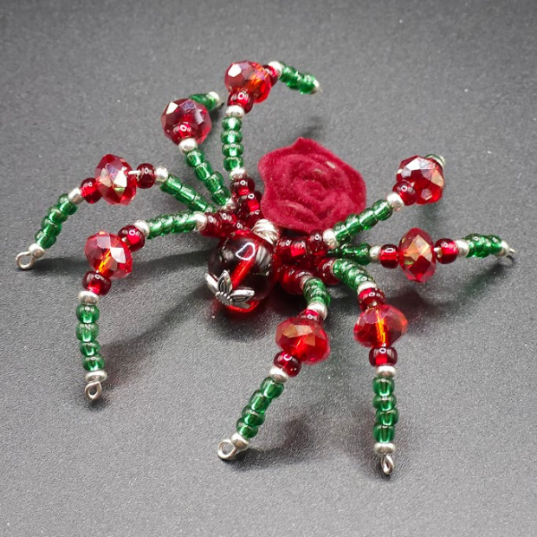 Beaded spider decoration with red, green, and black beads, and a red velvet body on a dark surface.