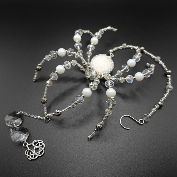 A jewelry set featuring a beaded spider brooch with pearl and crystal beads and a matching necklace with a crystal pendant and a silver Celtic knot charm.