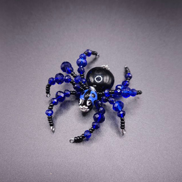 Beaded spider with black and blue beads and a black bead body, displayed on a gray surface.