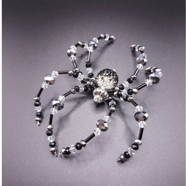 A spider made of black and clear beads and a central clear, rhinestone-encrusted bead for the body, placed on a dark surface.