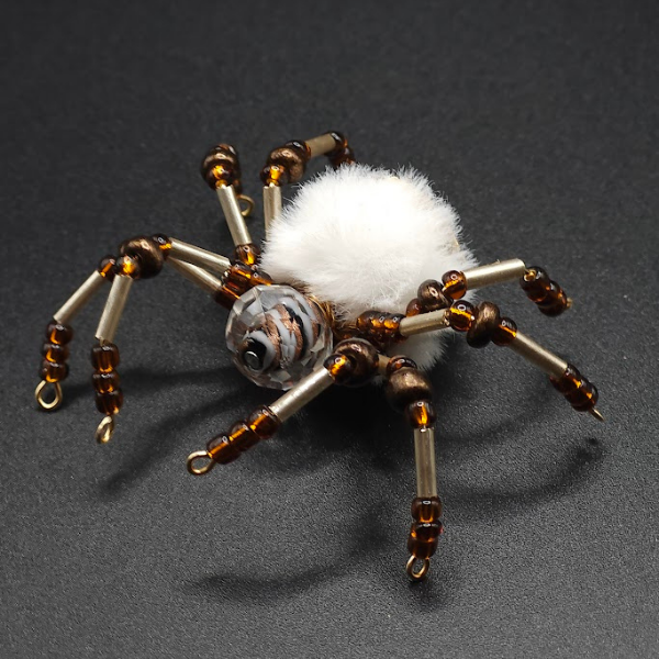 A spider-shaped ornament with beaded legs and a fluffy white body on a black background.