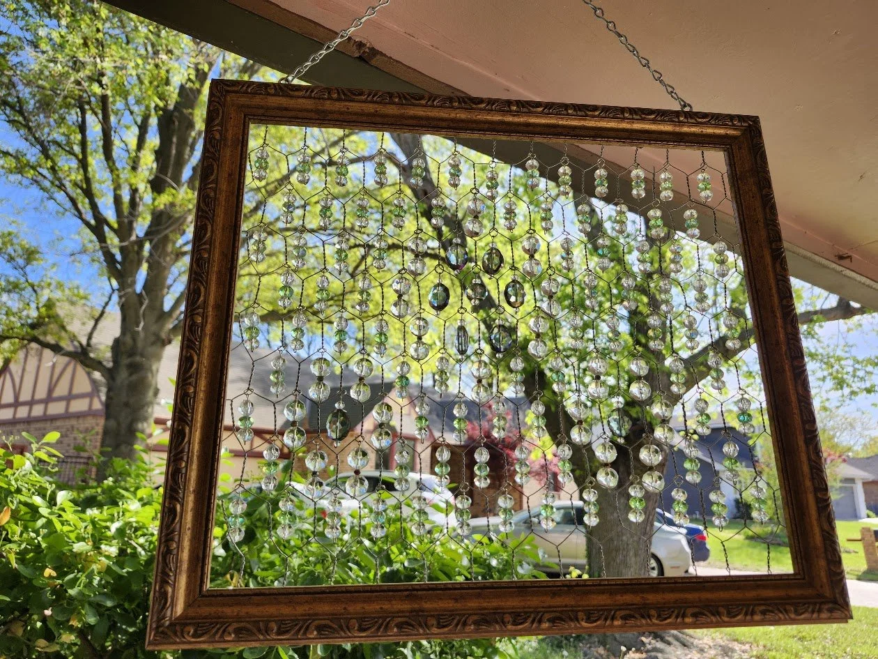 Decorative suncatcher made with a picture frame with hanging beads reflecting trees and houses