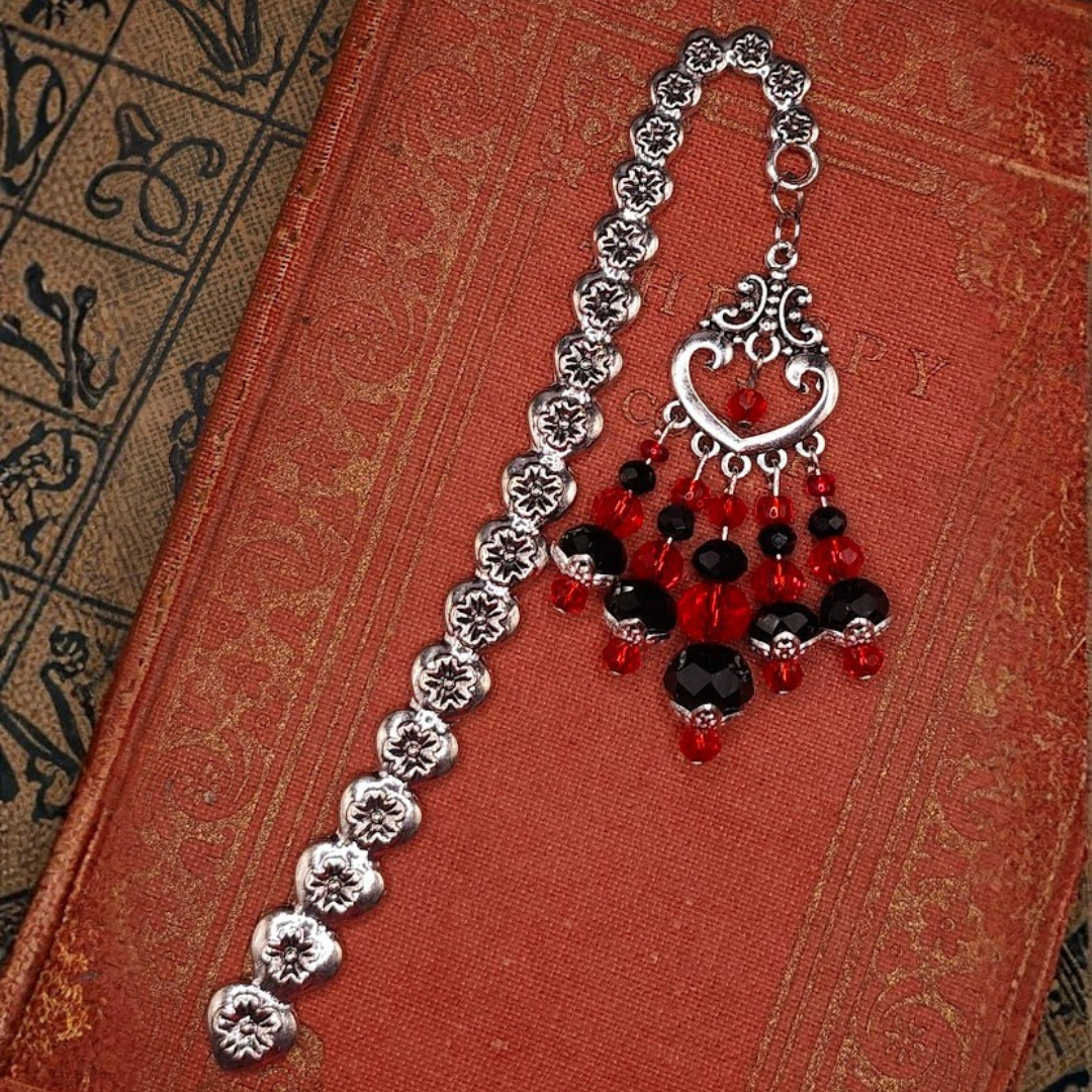 Vintage silver bookmark with floral design and red and black beads, placed on an ornate red book cover.