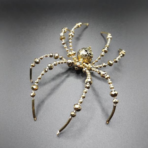 Gold-colored jewelry designed to resemble a spider with multiple articulated legs decorated with small beads.