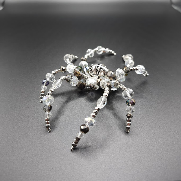 A silver spider-shaped ornament decorated with clear crystal beads and rhinestones, lying on a black surface.