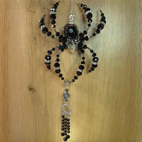 Decorative spider-shaped jewelry piece with black beads and silver accents hanging against a wooden background.